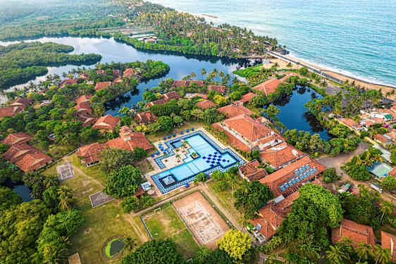 Luftfoto av en resort med terrakottafärgade tak, en stor pool och omgivande grönska. (AI-genererad text)