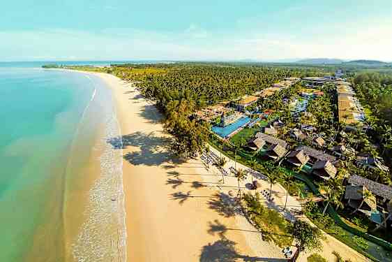 Flygfoto av en lång sandstrand med turkost vatten och en semesteranläggning med bungalower och pooler. (AI-genererad text)