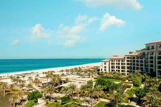 Utsikt över en resort vid havet med en byggnad, grönska och palmer i förgrunden. (AI-genererad text)