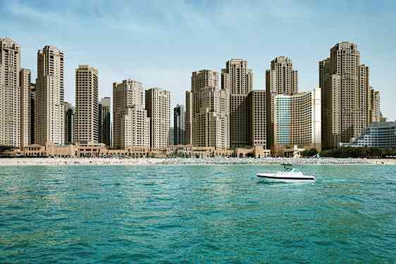En strandlinje med höga byggnader i bakgrunden och en båt på havet. (AI-genererad text)