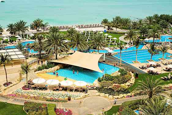 En badort med poolområde nära stranden, omgiven av palmer och solstolar. (AI-genererad text)