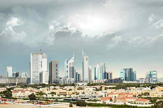 Bild av en stad med höga modernistiska byggnader i bakgrunden och låga byggnader med rödaktiga tak i förgrunden. (AI-genererad text)