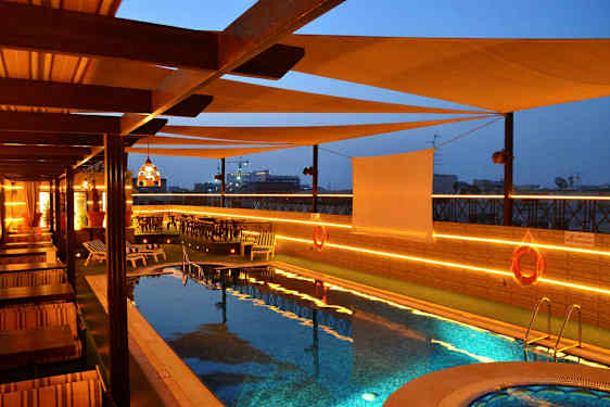 En pool på en terrass med solstolar och bord, med belysning på kvällen. (AI-genererad text)