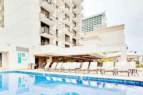 Bild av en byggnad med balkonger, en pool och solstolar. (AI-genererad text)