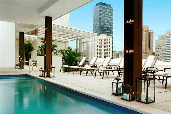 En modern utomhuspool med solsängar och tända lyktor i en stadsmiljö. (AI-genererad text)