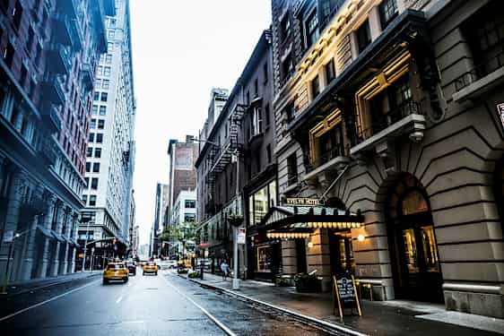 En stadsgata med höga byggnader längs sidorna och taxibilar som kör på vägen. Skylten för Evelyn Hotel syns till höger. (AI-genererad text)