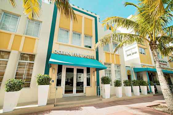 En hotellfasad med turkost tak och gula detaljer omgiven av palmer. (AI-genererad text)