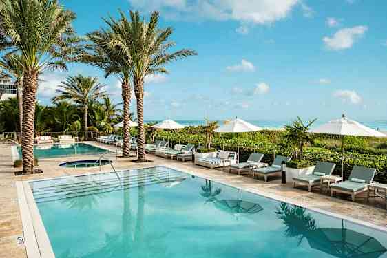 Bild av ett hotellpoolområde med palmer, solsängar och parasoller vid kanten. Havet är synligt i bakgrunden. (AI-genererad text)