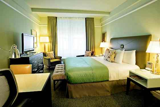 Ett hotellrum med en stor säng, ett skrivbord och en TV. Rummet är inrett i gröna toner och har stora fönster. (AI-genererad text)