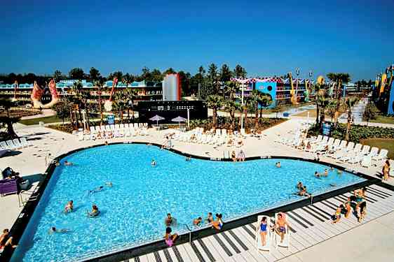 En simbassäng omgiven av solstolar vid ett semesterresort. Bakgrunden visar byggnader och dekorationer. (AI-genererad text)