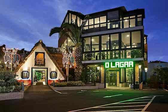 En byggnad med en traditionell stråtaksvit och en modern glaspanel struktur bredvid, upplyst på kvällen med lysande dekorationer och markbelysning. (AI-genererad text)