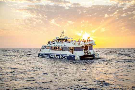 En glasbottenbåt med människor ombord åker på havet under en solnedgång. (AI-genererad text)