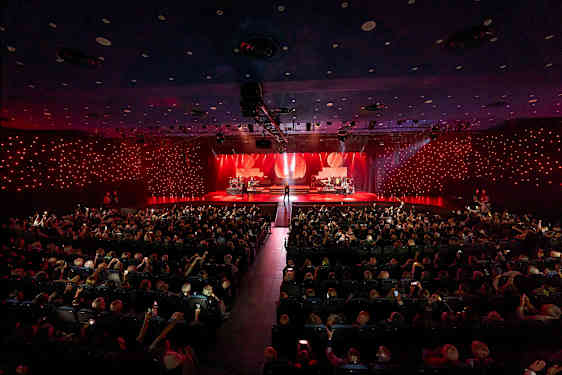 En konsertsal med en upplyst scen där olika musiker framträder inför en publik. (AI-genererad text)