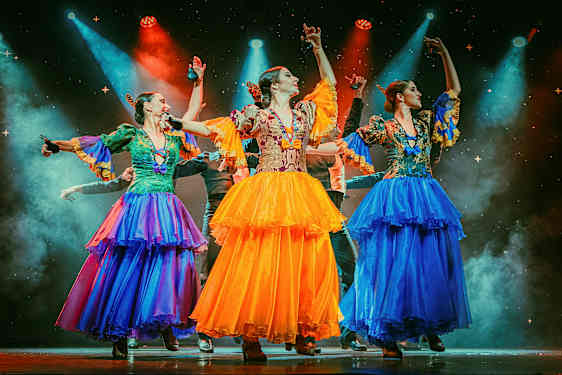 Tre personer klädda i färgglada traditionella dräkter dansar på en upplyst scen. (AI-genererad text)