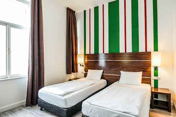 Ett hotellrum med två enkelsängar, bruna gardiner och en vägdesign med gröna, vita och röda ränder. (AI-genererad text)