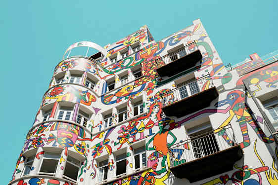Byggnad med färgglada abstrakta målningar på fasaden mot en klarblå himmel. (AI-genererad text)