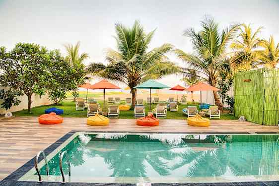 En pool med solsängar och färgglada parasoller i en trädgård omgiven av palmer. (AI-genererad text)