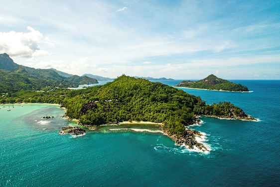 Flygfoto av en grönskande ö omgiven av klarblått hav och mindre öar i bakgrunden. (AI-genererad text)