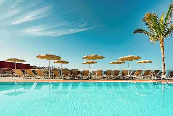 En pool med solstolar och parasoller under en klar blå himmel. (AI-genererad text)