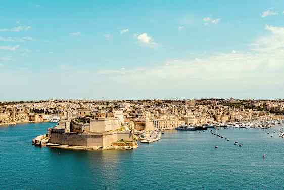 Vy över en kuststad med historiska byggnader och hamn. (AI-genererad text)