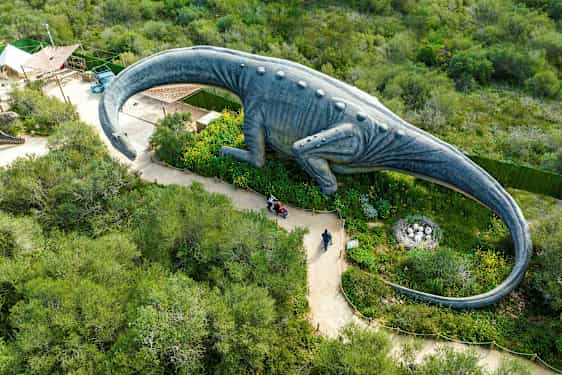 En stor dinosauriestaty omgiven av grönska sedd ovanifrån. (AI-genererad text)