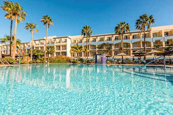 En utomhuspool omgiven av palmer och ett hotell i bakgrunden. (AI-genererad text)