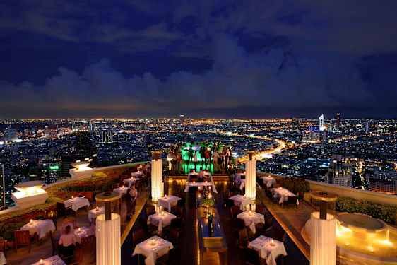 En takterrassrestaurang på kvällen med upplysta bord och utsikt över en stad med lysande ljus. (AI-genererad text)