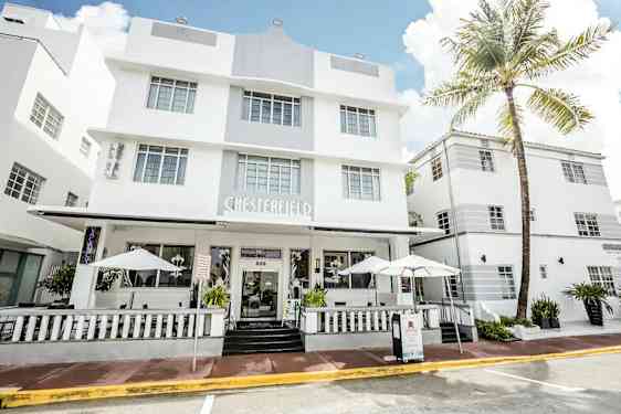 Ett vitt hotell i en modern arkitekturstil med stora fönster och en veranda med parasoll. (AI-genererad text)