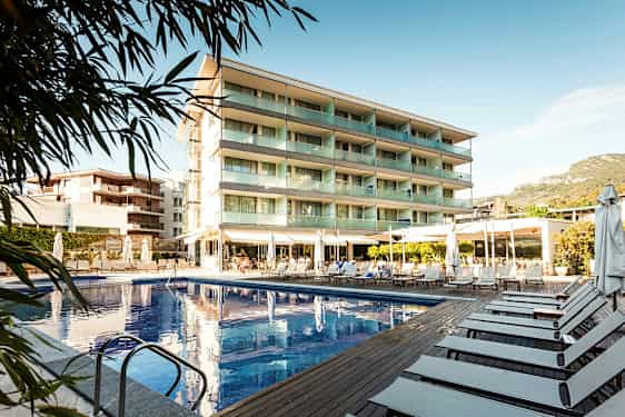 Bild av ett hotell med swimmingpool och solstolar utomhus. (AI-genererad text)