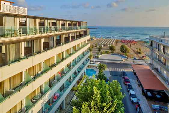 En hotellbyggnad med balkonger, en gata med parkering och trottoar, samt en strand med solstolar och havet i bakgrunden. (AI-genererad text)