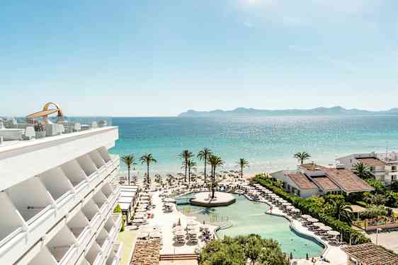 En utsikt över hotellpool, strand och hav med palmer och byggnader. (AI-genererad text)