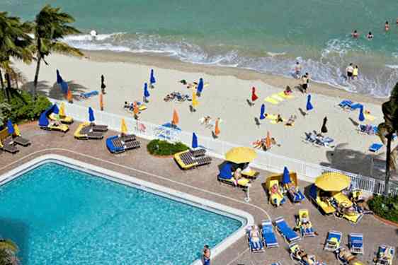 En strand med solstolar, parasoller och badande människor samt en pool med omgivande solstolar. (AI-genererad text)