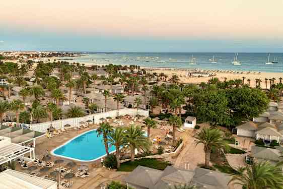 Luftbild av hotellområde med pool, palmer och en strand i bakgrunden. (AI-genererad text)