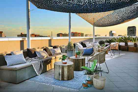 En takterrass med sittmöbler, bord och korgar dekorerade med växter och kuddar är avbildad. (AI-genererad text)