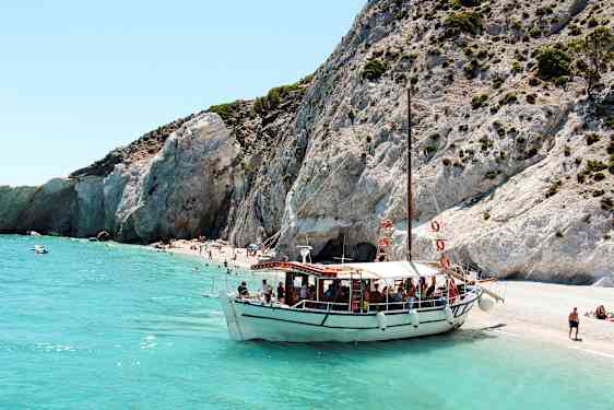 En båt ligger förtöjd vid en strand med klippor och klart turkosblått vatten. (AI-genererad text)