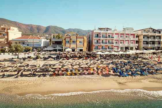 Strand med parasoller framför flerfärgade byggnader. (AI-genererad text)