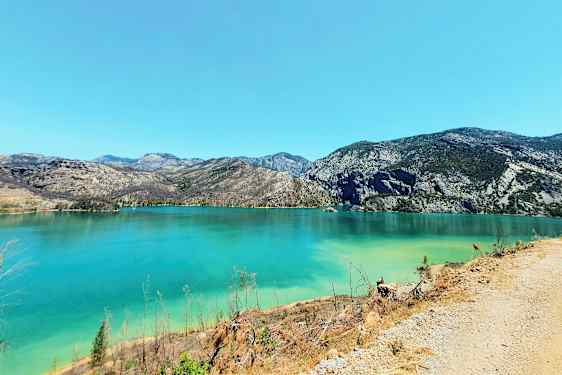 En bild föreställer en klar turkos sjö omgiven av berg under en molnfri himmel. (AI-genererad text)
