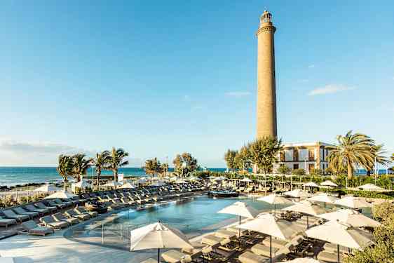 En solig resort med pool, solstolar och parasoller samt en fyr i bakgrunden. (AI-genererad text)