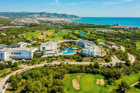 Flygbild över hotellkomplex med pooler, omgivande golfbanor och stadsvy mot kusten. (AI-genererad text)