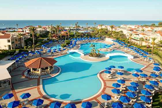 Utomhuspool med omgivande solstolar och parasoller samt hotellbyggnader i bakgrunden mot havet. (AI-genererad text)