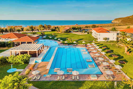 Utomhuspool med solstolar och parasoller, grönskande gräsmatta och hav i bakgrunden. (AI-genererad text)