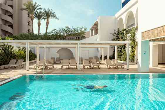 En utomhuspool med solstolar bredvid och en person som simmar i vattnet. (AI-genererad text)