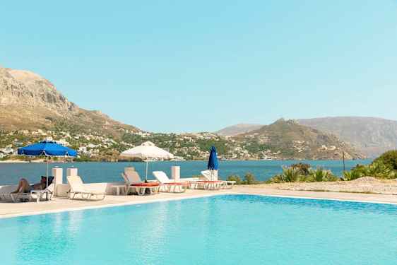 Utomhuspool med solstolar och parasoller, samt utsikt över hav och berg. (AI-genererad text)