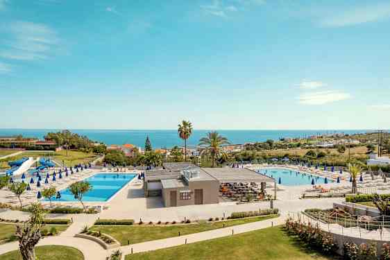 Hotellområde med två swimmingpooler, solstolar och havsutsikt. (AI-genererad text)