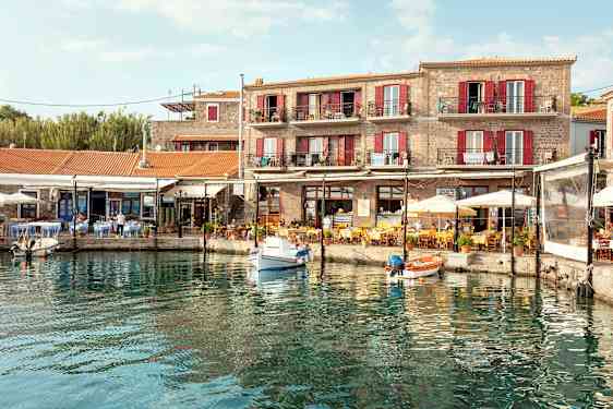 En hamn med små båtar, omgiven av en byggnad med terrasser och en restaurang med uteservering. (AI-genererad text)