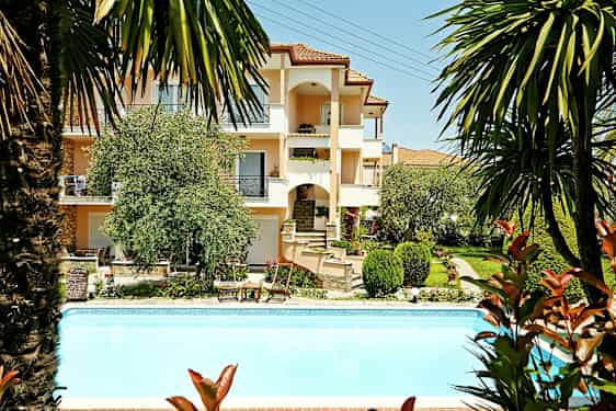 En byggnad med flera våningar omgiven av grönska och en pool i förgrunden. (AI-genererad text)