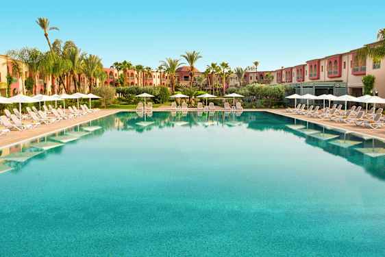 Stor pool med solstolar och parasoller vid kanterna, omgiven av palmer och byggnader. (AI-genererad text)