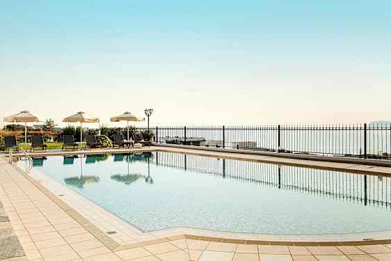 En utomhuspool med solsängar och parasoller vid sidan mot en bakgrund av havet. (AI-genererad text)