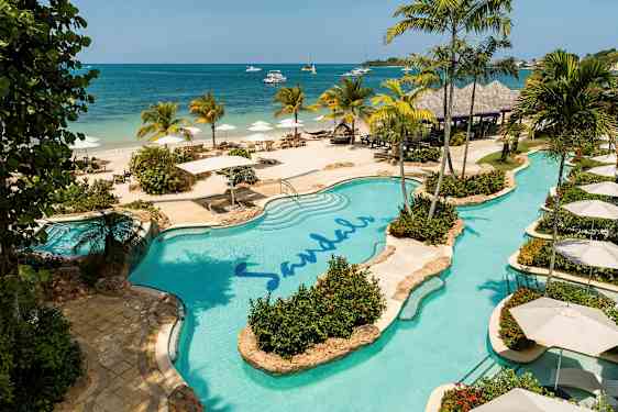 Poolområde vid stranden med palmer och parasoller. (AI-genererad text)