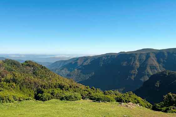 Bilden visar ett landskap med grönskande kullar och berg under en klar blå himmel. (AI-genererad text)